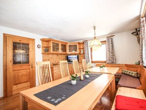 A cozy kitchen with wooden cabinets, a dining table with chairs, a bench, and a television.