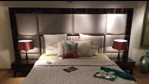 A neatly made bed with a patterned bedspread, two bedside lamps, and a bedside table with a lamp. - Jagannath B&B Hotel (New Delhi)