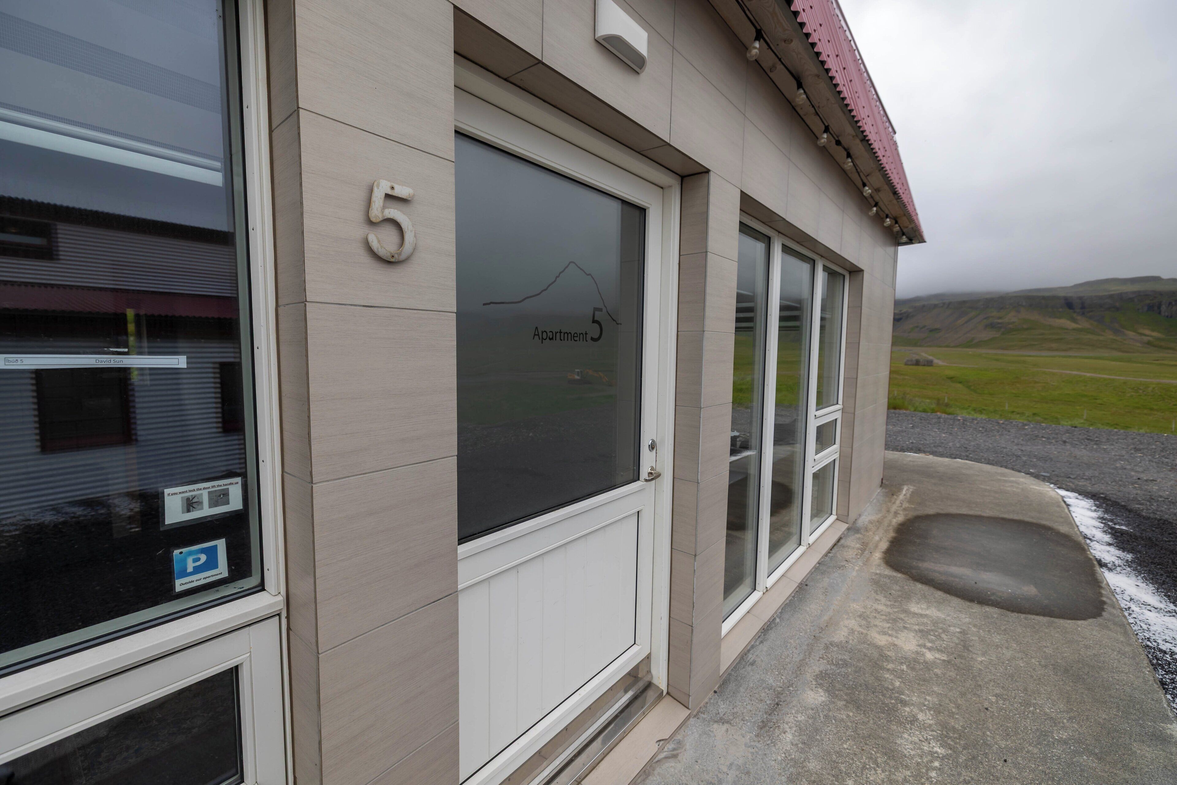 A building with a large window displaying 'Apartment 5' and a mountain view.