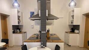 A compact kitchen with a central island, two pendant lights, a microwave, and a coffee maker. - Kirkjufell Guesthouse and Apartments (Grundarfjörður)