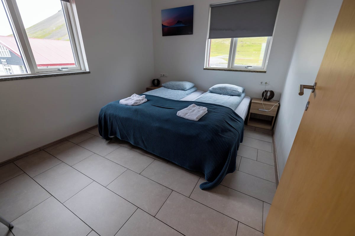 Une chambre à coucher avec un lit, deux tables de chevet, une fenêtre et un tableau au mur.