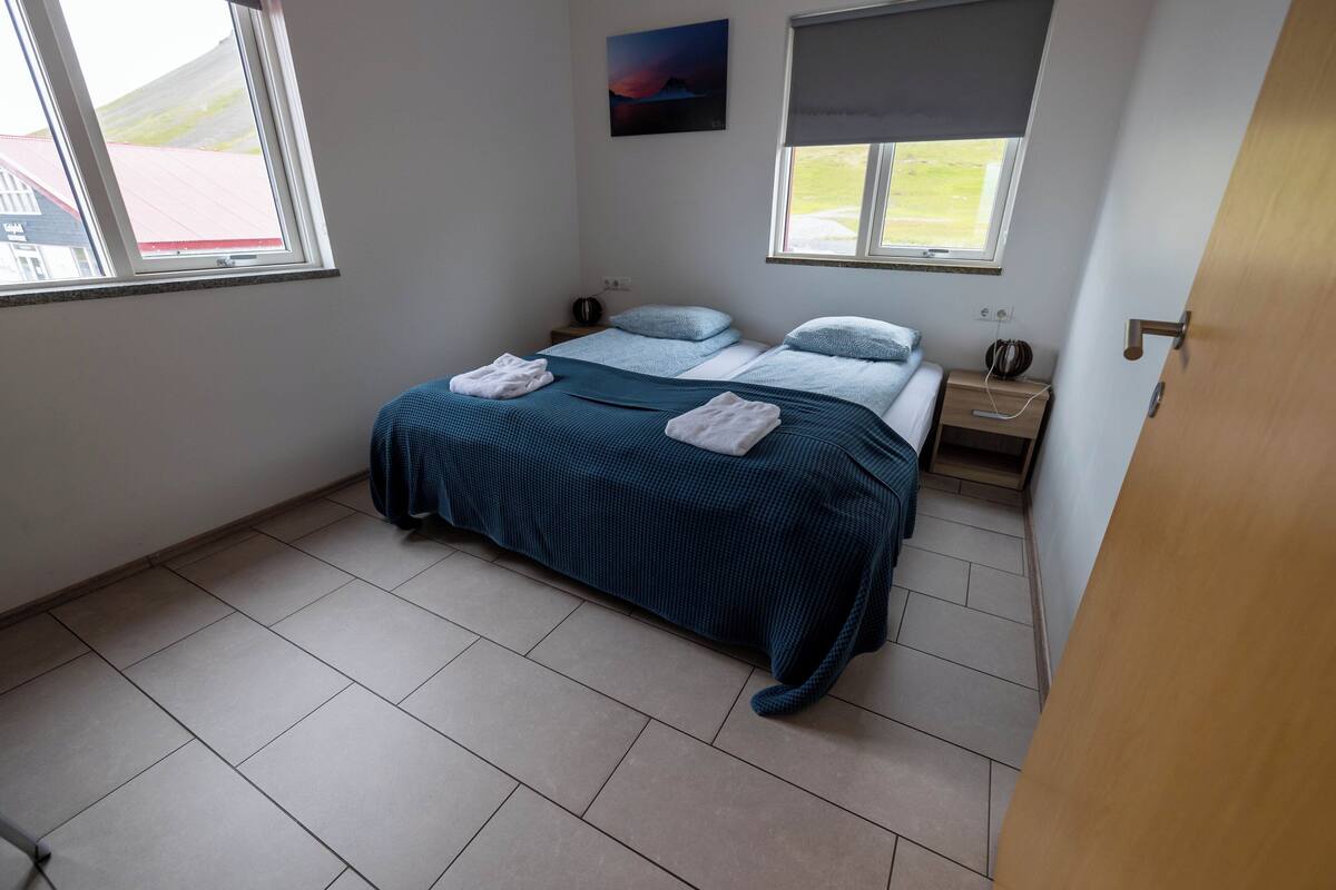 Un dormitorio con una cama, dos mesitas de noche, una ventana y un cuadro en la pared.