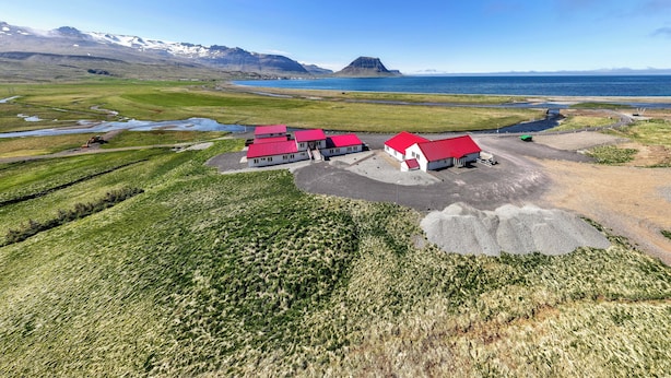 A rural area with a cluster of red-roofed buildings, a large body of water, and mountains in the background. - Kirkjufell Guesthouse and Apartments (Grundarfjörður)