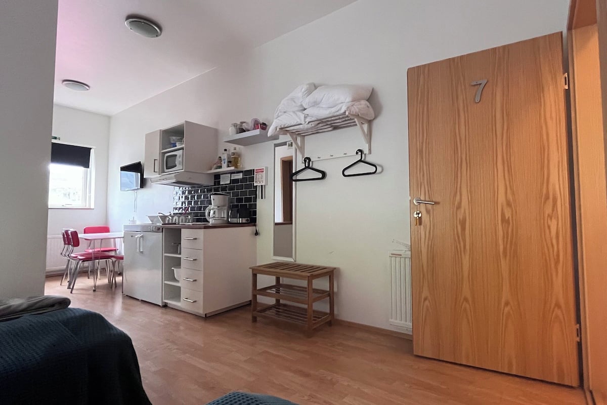 Une pièce de taille modeste comprenant un coin cuisine, une porte en bois et une petite table.