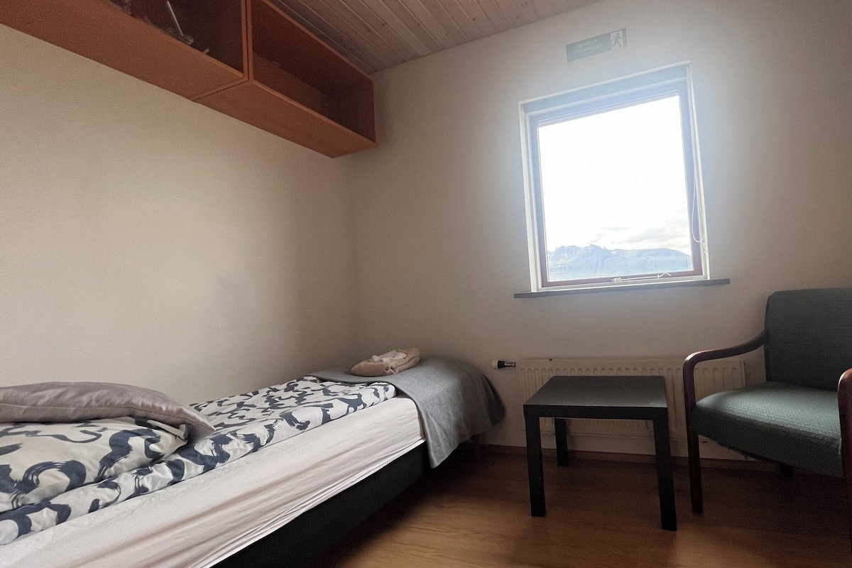 Une petite pièce avec un lit, une chaise et une fenêtre.