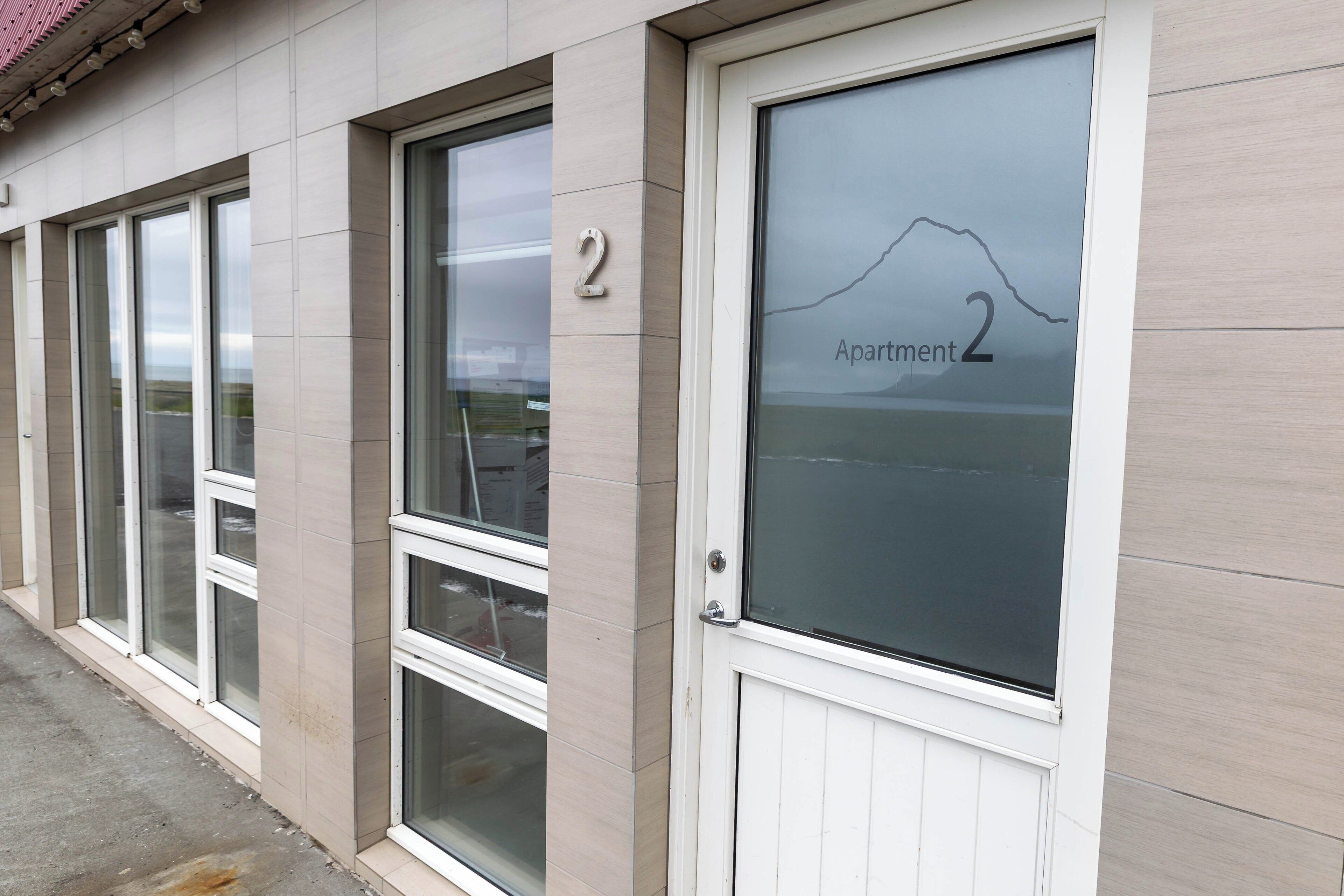 A building facade with a numbered door labeled "Apartment 2" and a window with a mountain view.
