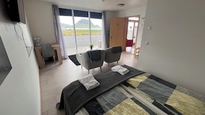 A hotel room with a bed, two chairs, a desk, and a view of a lake and mountains. - Kirkjufell Guesthouse and Apartments (Grundarfjörður)