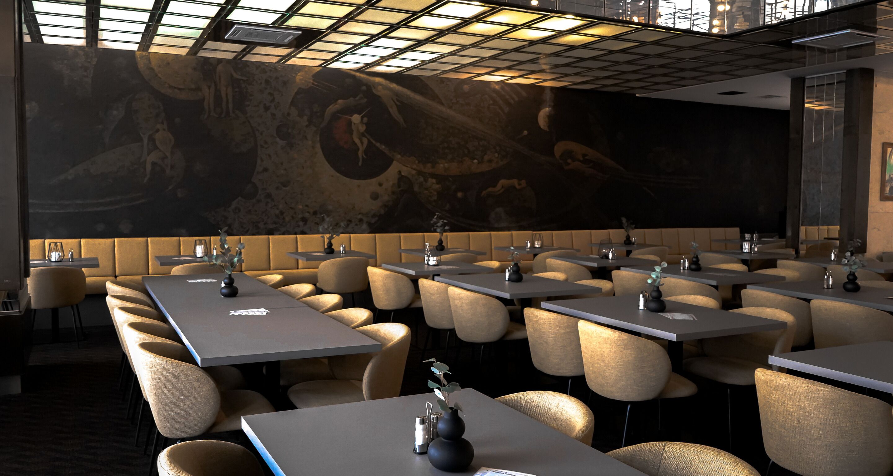 A modern restaurant with a high ceiling, recessed lighting, and a large mural on the back wall. Tables are arranged in a U-shape, and the chairs are upholstered in a light fabric.