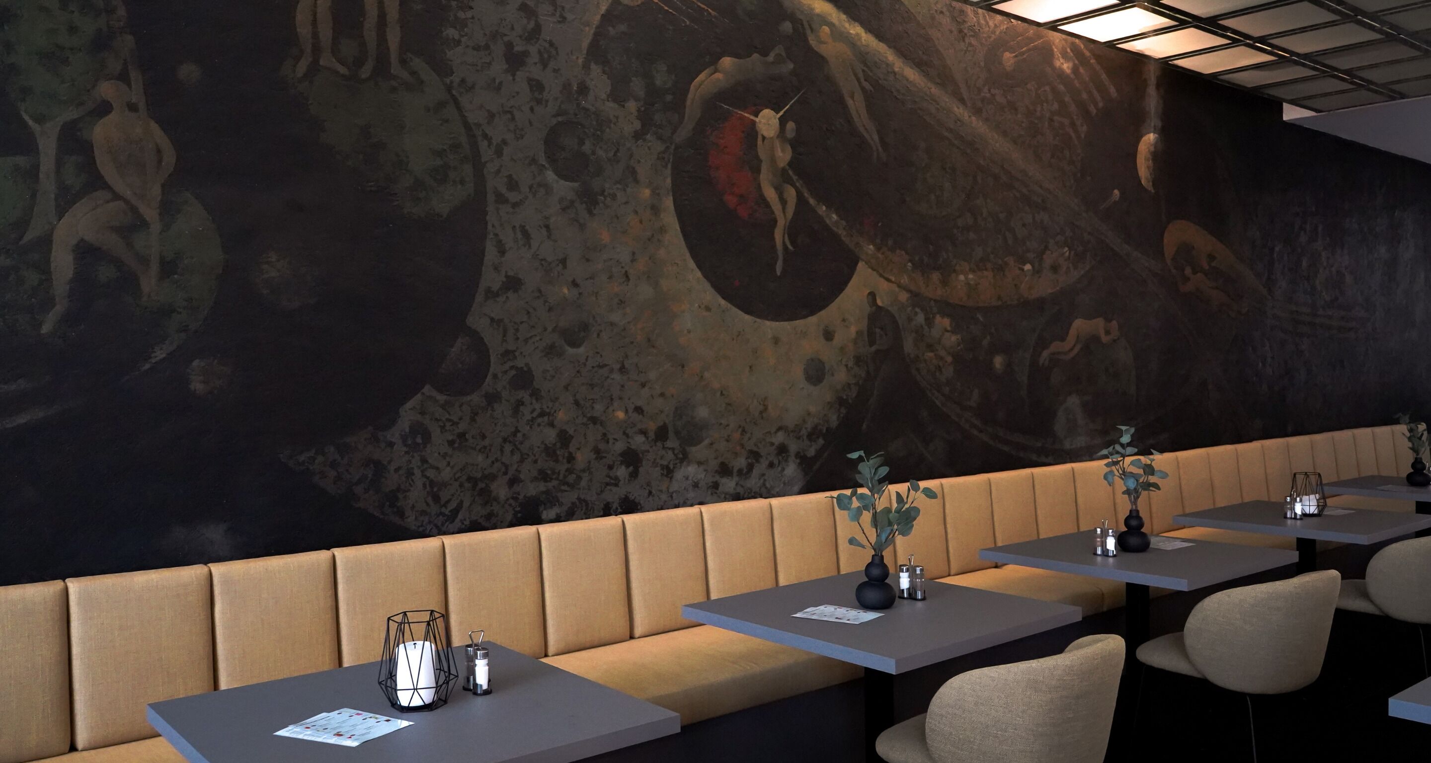 A restaurant with booths and tables, a mural on the wall, and a ceiling with lights.