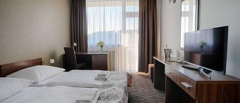 Habitación de hotel con dos camas, un escritorio, un televisor y una ventana con cortinas.