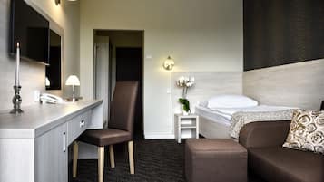 A hotel room with a desk, chair, bed, and a small table with a plant.