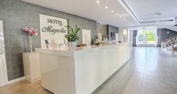 Zona de recepción de un hotel con diseño moderno, una amplia mesa de recepción, un cartel en la pared y una escalera que sube a otro piso.