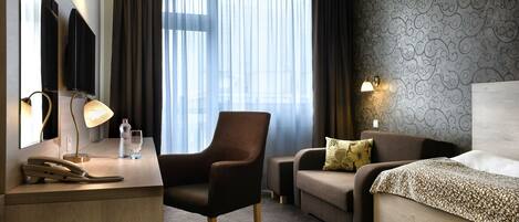 A hotel room with a desk, chair, sofa, and bed. There are two bedside lamps, a mirror, and a window with curtains.