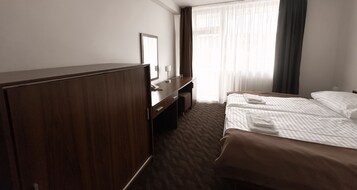 Una habitación de hotel con un armario de madera, un escritorio con espejo, un teléfono y una cama con sábanas ordenadas.