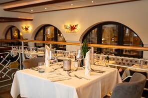 Een restaurant met gedekte tafels, een balkongevel en boogvensters.