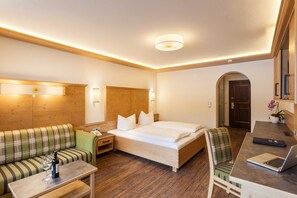 Une chambre d’hôtel avec un lit, un canapé, un bureau avec un ordinateur portable, une bouteille de vin et une lampe.