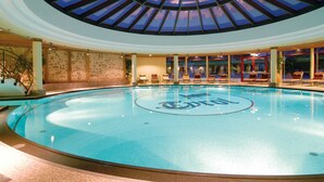 Ein Innenpool mit Glasdecke, Steinwänden und Liegestühlen rundherum.