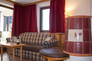 Un salon avec un canapé à carreaux, une table en bois sur laquelle sont posés des verres à vin, et un mur d’accent de couleur rouge.