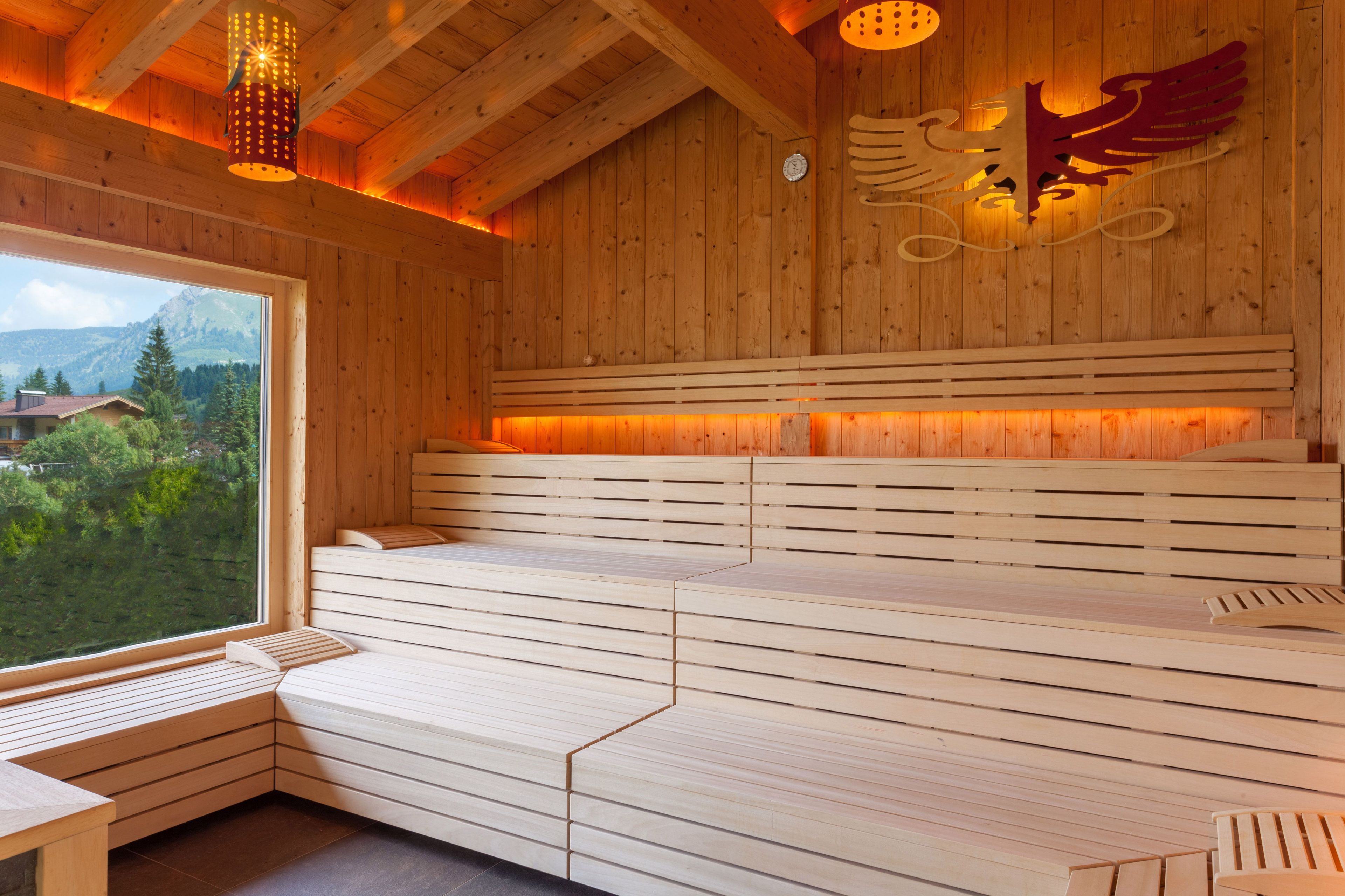 A wooden sauna with benches, a large window, and a decorative wall piece.