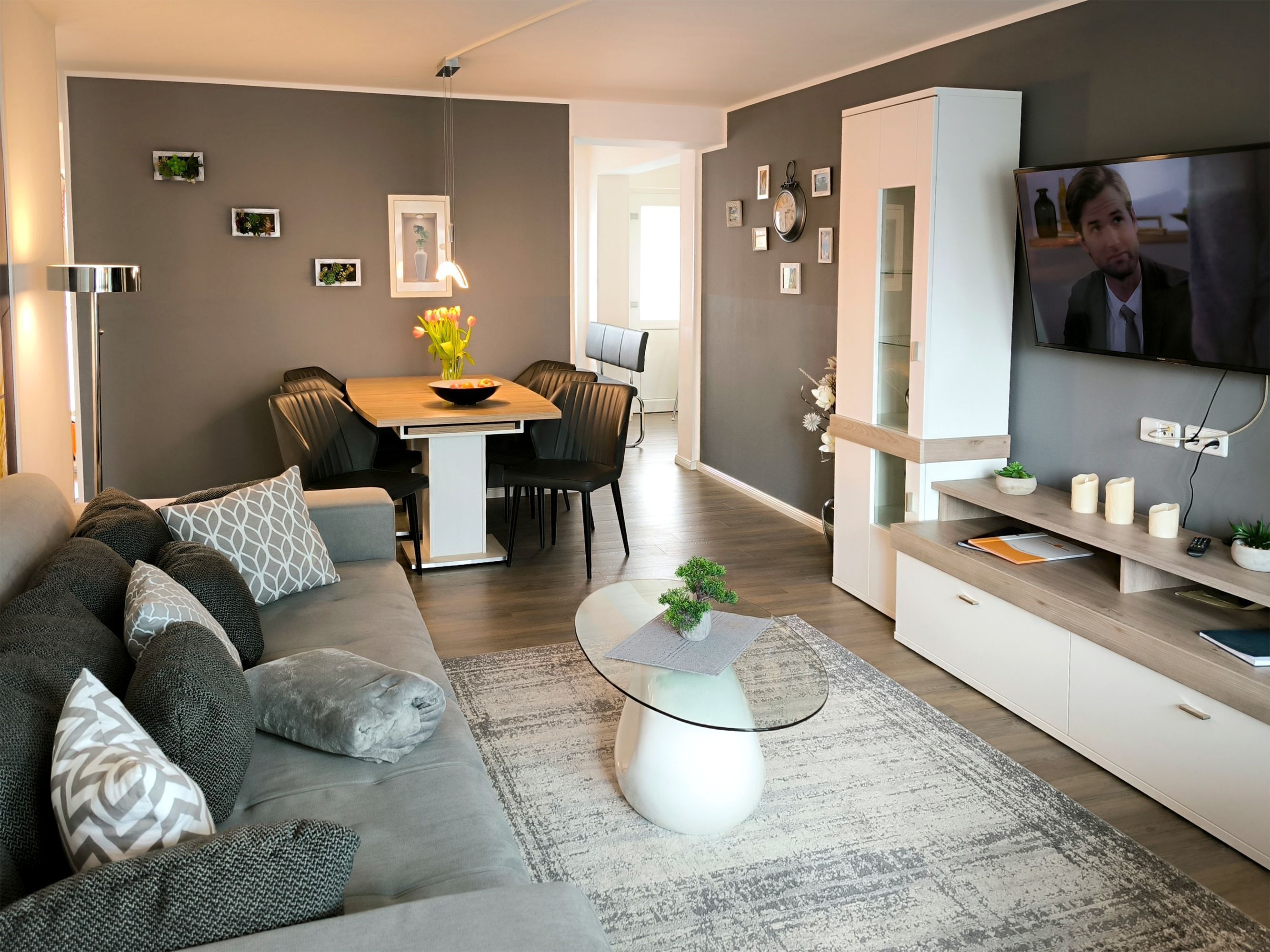 A modern living room with a sofa, coffee table, TV, and dining area.