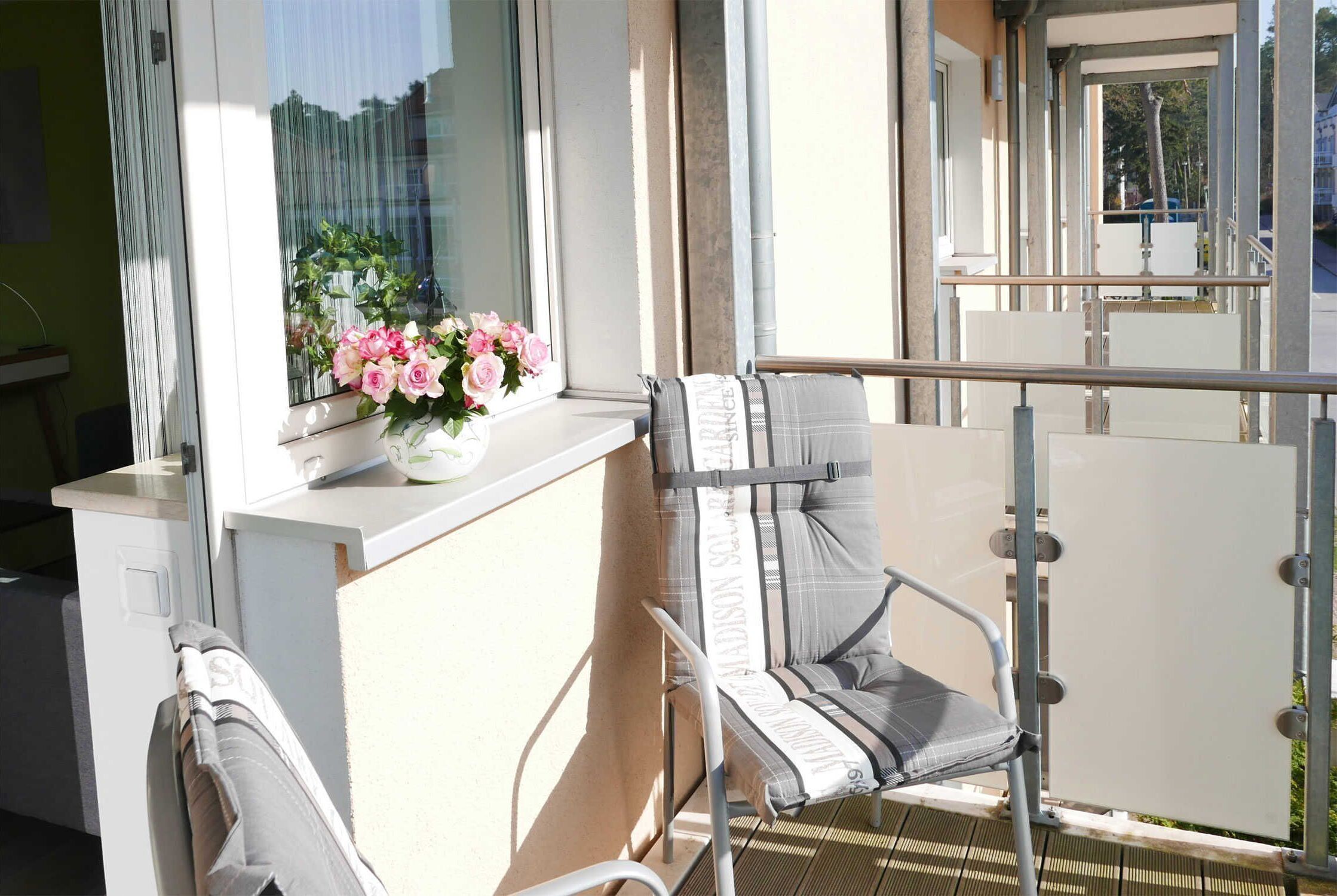 Un balcon avec une chaise, une fenêtre agrémentée d’un arrangement floral et une rambarde.