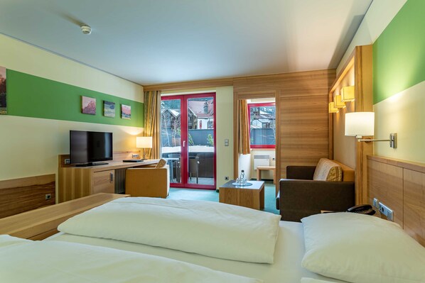 Habitación de hotel con cama, escritorio con televisor, una silla y vista a través de un ventanal.