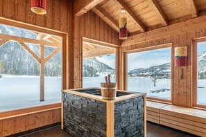 A wooden cabin with large windows, a stone fireplace, and a view of a snowy landscape. - Family room Esche - Hotel Tyrol am Haldensee (Haldensee)