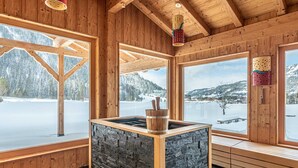 A wooden cabin with large windows, a stone fireplace, and a view of a snowy landscape.