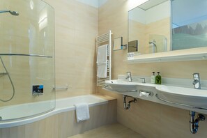 A modern bathroom with a glass-enclosed shower, a bathtub, and two sinks.