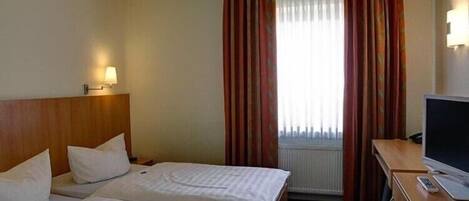 Una habitación de hotel con dos camas, un televisor sobre una mesa de madera y una ventana con cortinas.
