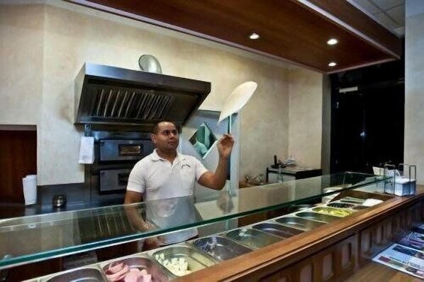 A buffet area with a glass partition, various food containers, and a person holding a menu.
