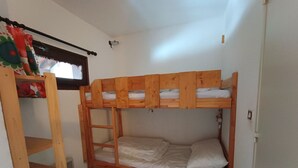 Cameretta con letto a castello, scala in legno, un piccolo ripiano e finestra con tende.