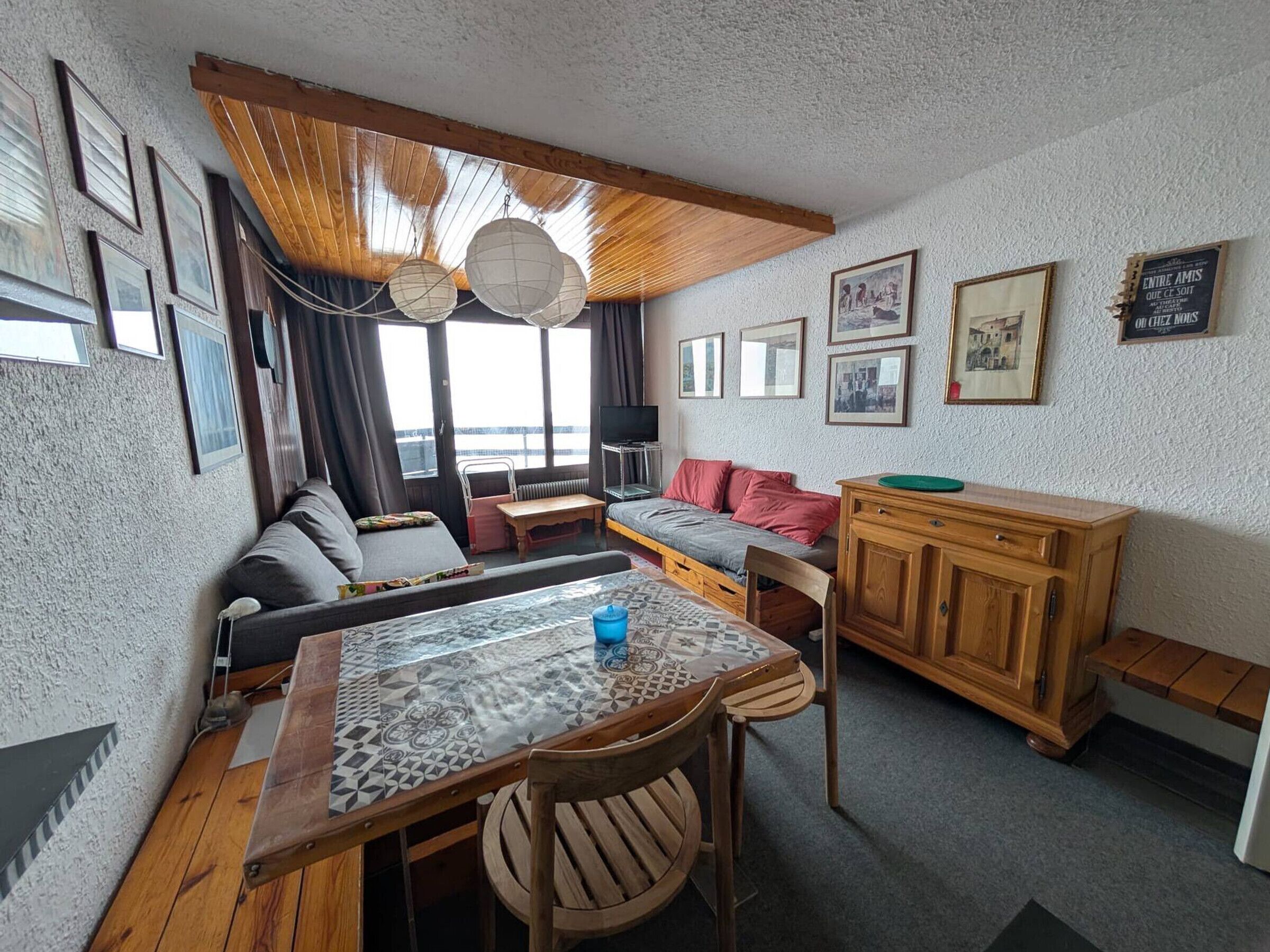 A cozy room with a sofa, a dining table with chairs, a wooden cabinet, and a view of the sea through large windows.