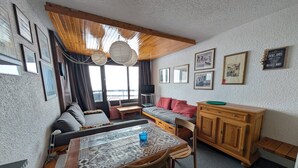 Una camera accogliente con un divano, un tavolo da pranzo con sedie, un armadietto in legno e vista sul mare attraverso ampie finestre.