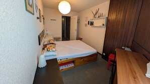 Una stanza piccola e accogliente con un letto singolo, una panca di legno, un tavolino e uno scaffale con oggetti decorativi.