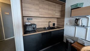 Una cucina compatta con forno a microonde, tostapane, lavello e bollitore su uno scaffale.