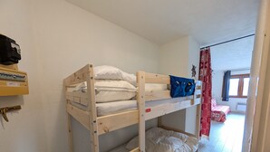 A bunk bed room with a wooden frame, a shelf with a black object, and a window with curtains. - Ski-in studio with washing machine for 4, pets allowed (Montgenèvre)