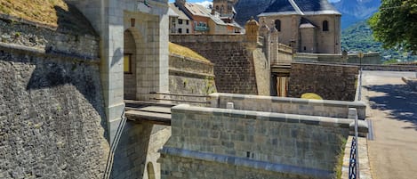 A stone bridge connecting two parts of a historic town, with old buildings and a church in the background.