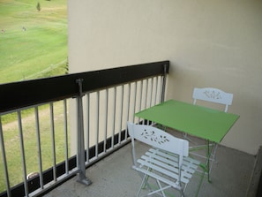Ein Balkon mit einem grünen Tisch und weißen Stühlen, mit Blick auf eine Rasenfläche.