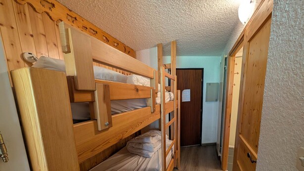 A bunk bed room with wooden walls and a door leading to another room.