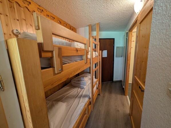 A bunk bed room with wooden walls and a door leading to another room.