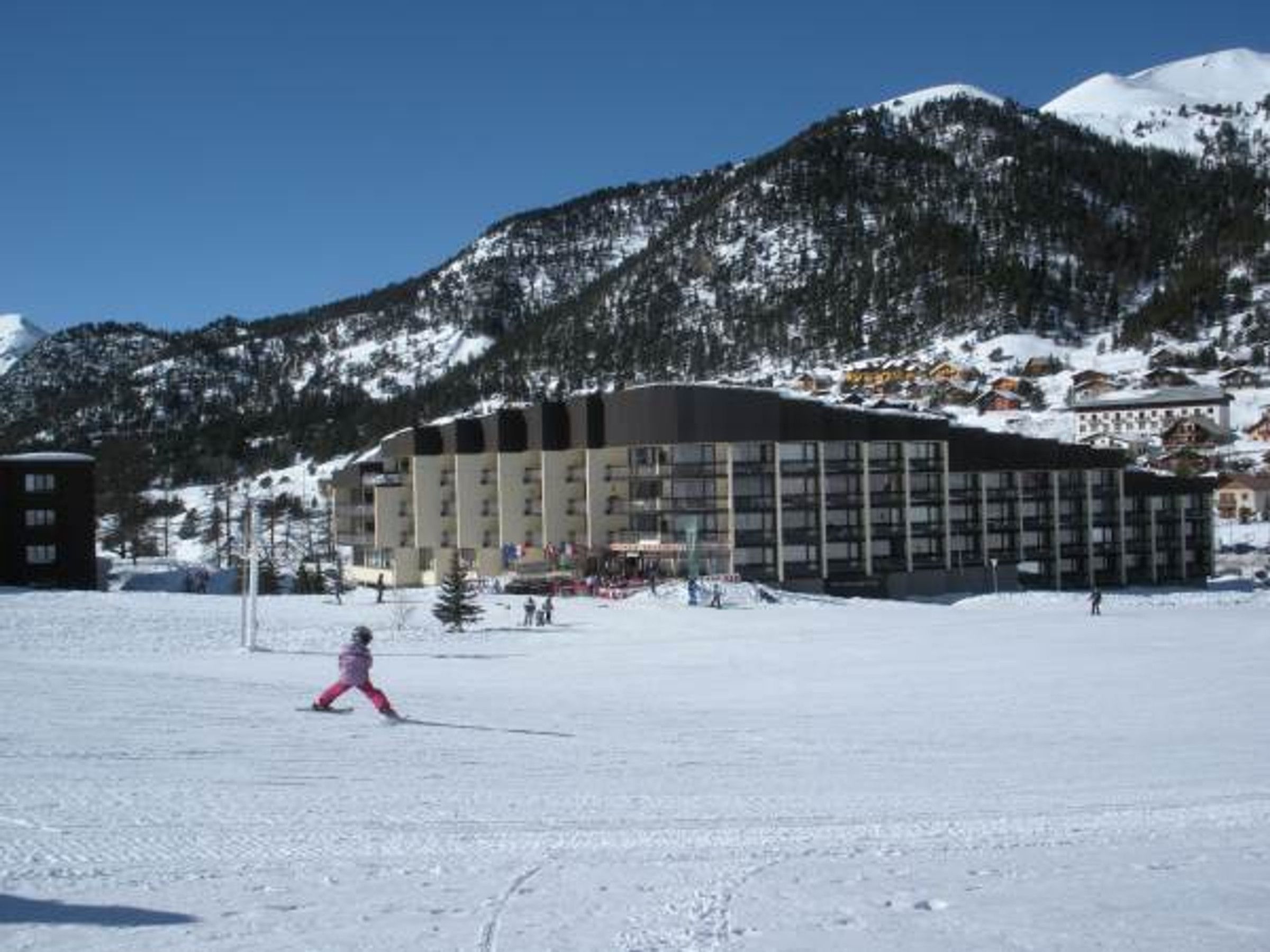Un grand bâtiment à étages, probablement un hôtel, entouré de montagnes enneigées et surplombant un ciel dégagé.