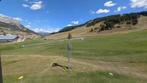 A grassy field with a clear sky, a mountain in the background, and a building with a sloped roof.