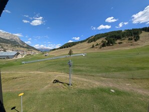 A grassy field with a clear sky, a mountain in the background, and a building with a sloped roof.