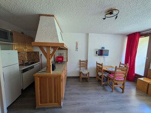 A compact kitchen with a refrigerator, stove, and wooden counter. There is a dining area with a table and chairs, and a television mounted on the wall.