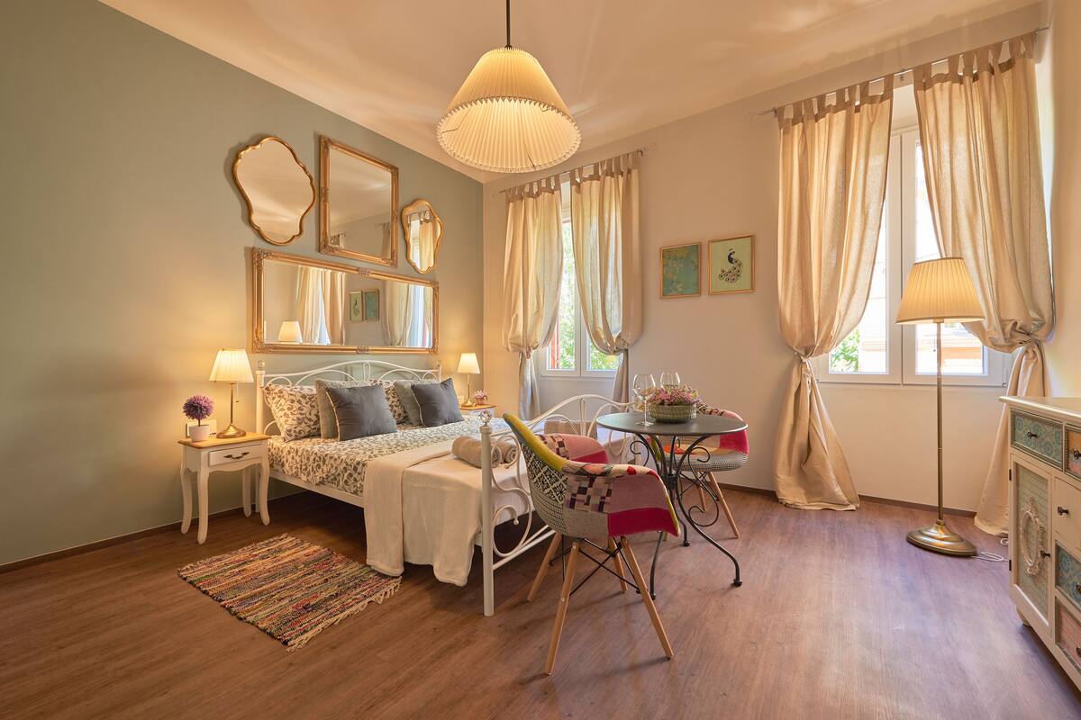 A bedroom with a bed, bedside tables, a chair, a lamp, a mirror, and curtains.