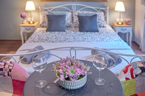 A neatly made bed with a patterned bedspread, two bedside lamps, and a small table with a potted plant and two wine glasses. - Old City Romantic Studios (Pula)