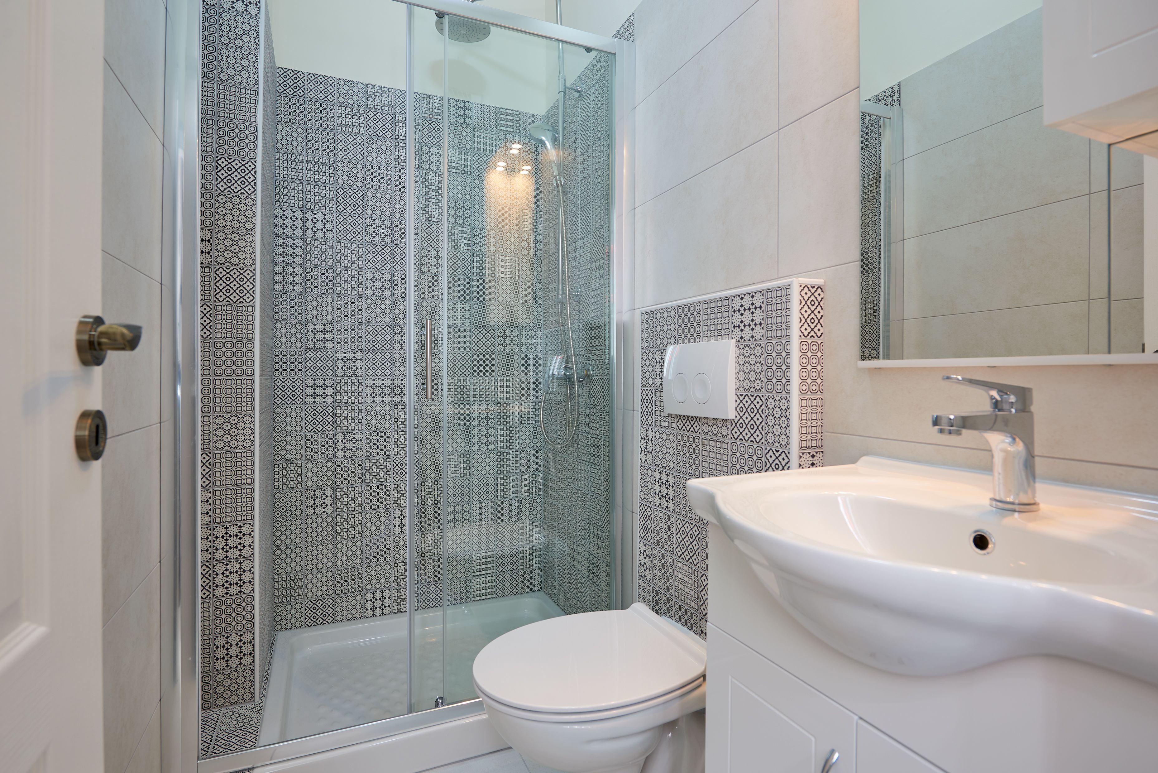 A bathroom with a glass-enclosed shower, a white toilet, and a sink with a mirror above it.
