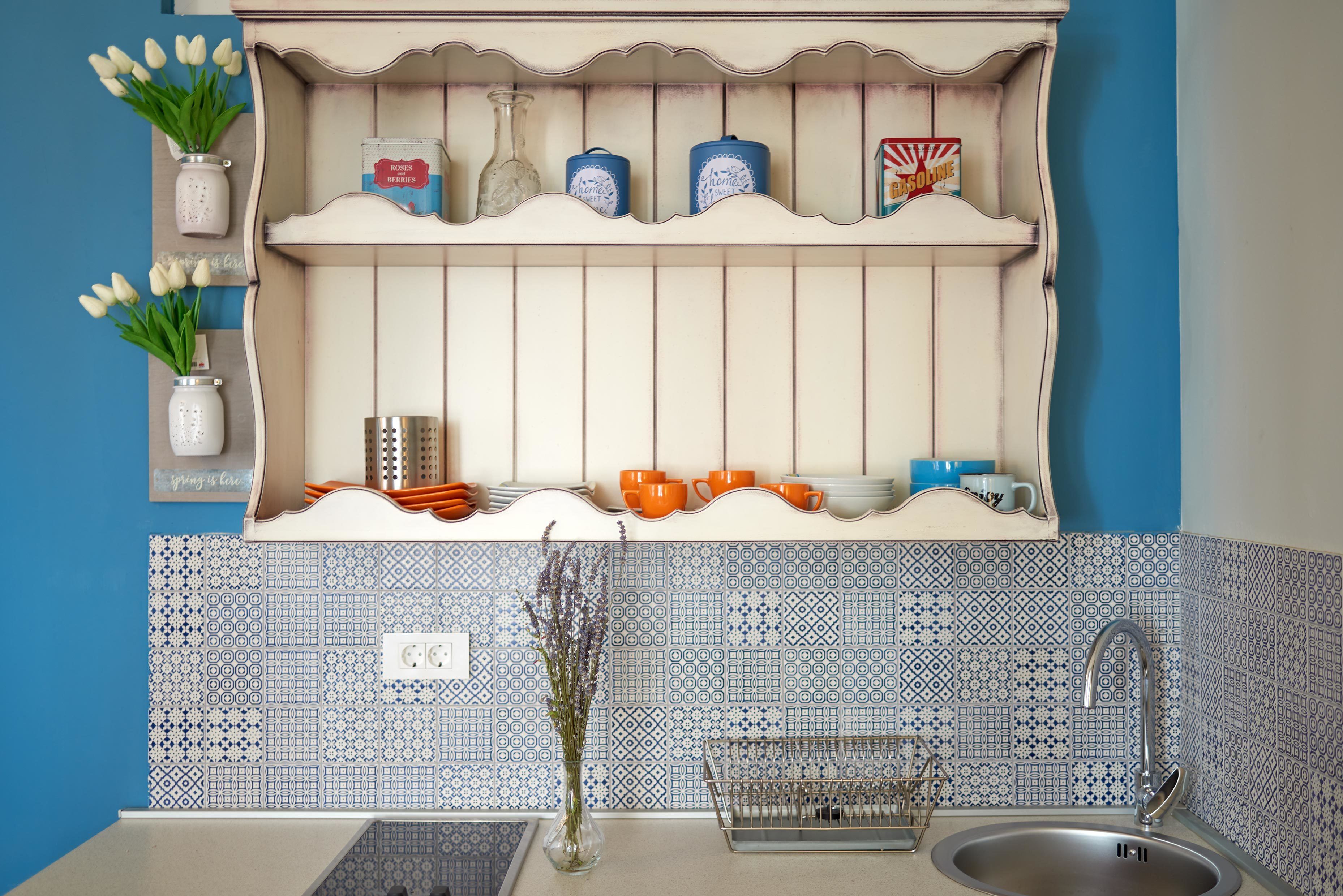Een keuken met een achterwand in wit en blauw, een gootsteen en planken met decoratieve objecten en keukengerei.