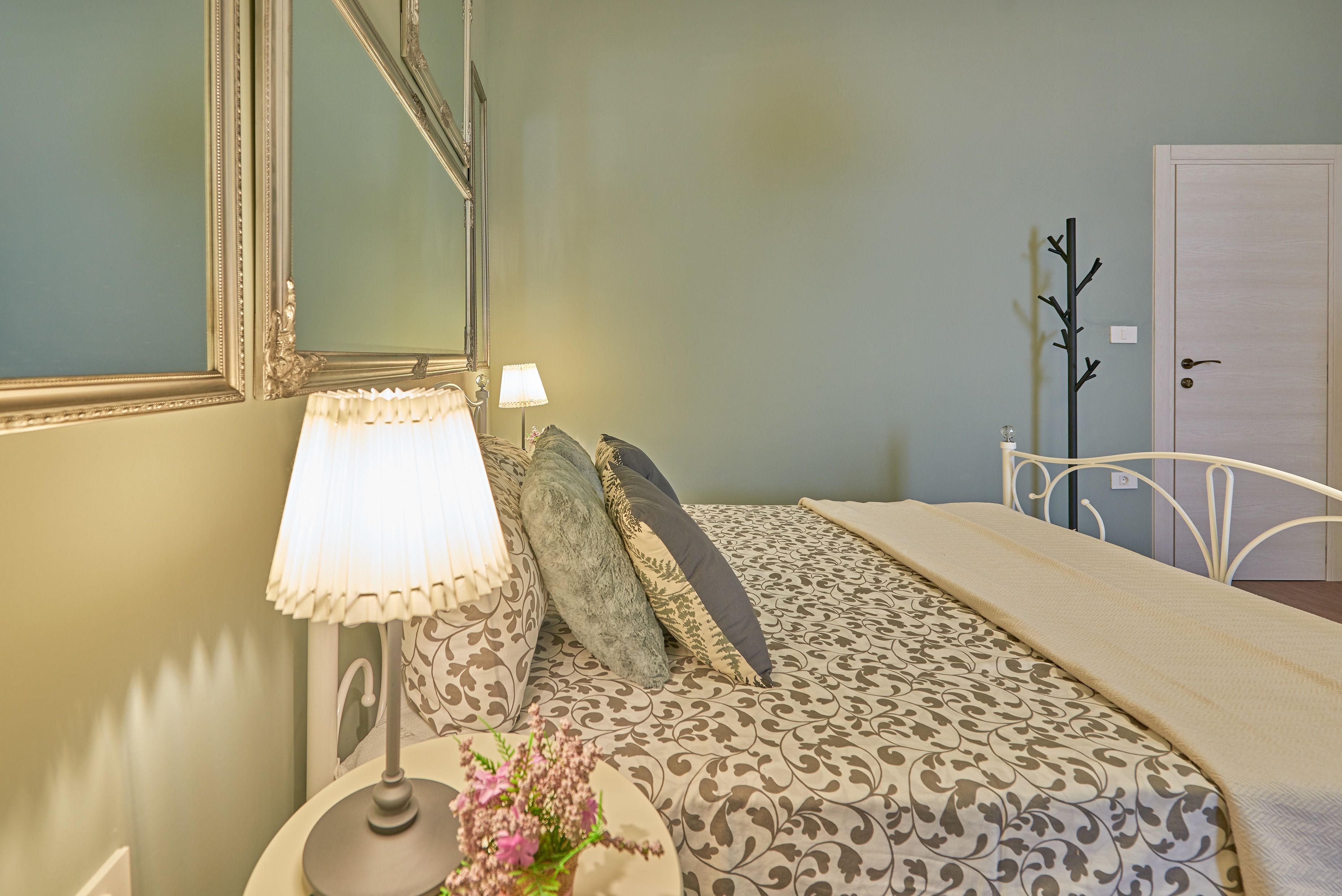 A neatly made bed with patterned bedding, a bedside lamp, and a mirror on the wall.